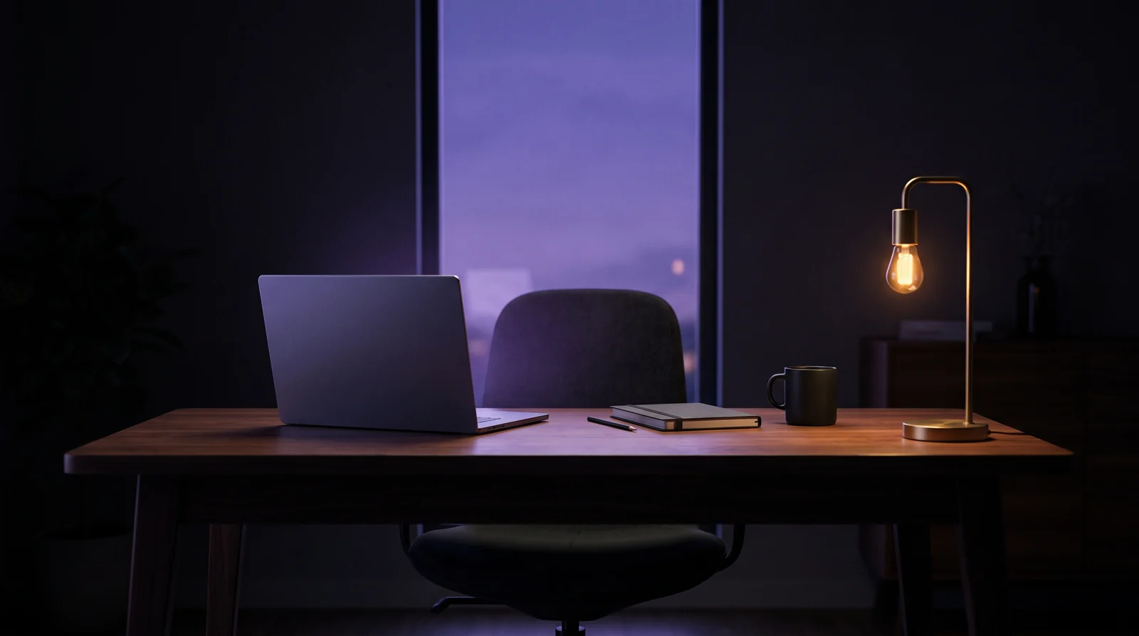 A laptop and a mug on a wooden desk by a window at dusk, lit by a brass desk lamp