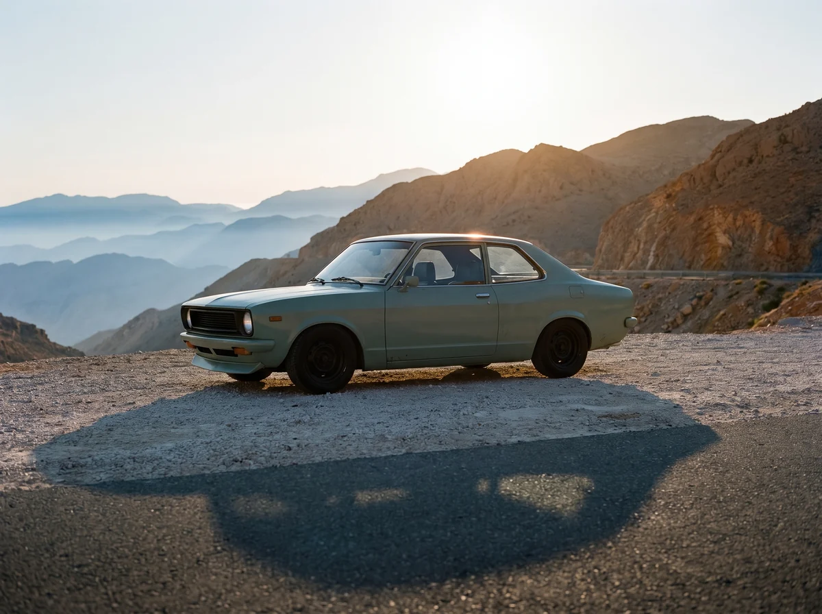 The coupe parked on gravel at the top of the road, the low sun behind it on the ridge, its shadow long