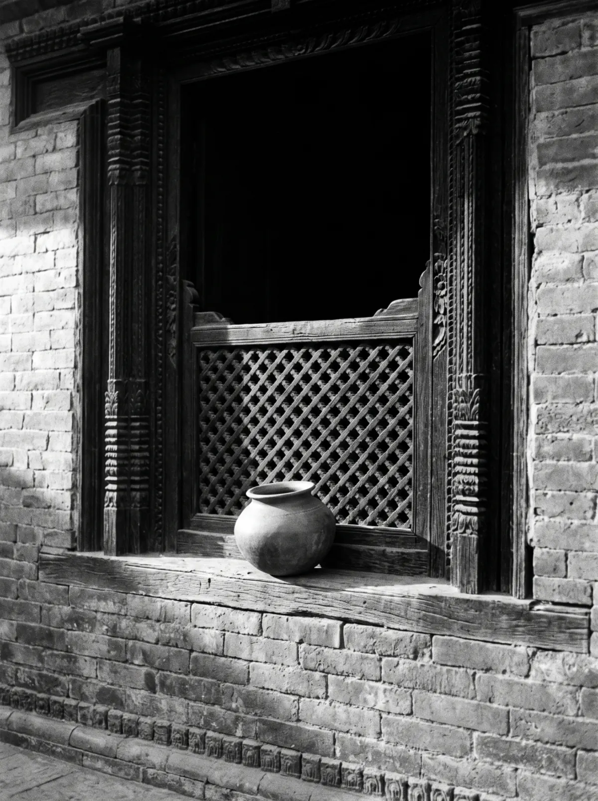 A carved wooden window with a lattice screen and a clay pot on the sill, lit from the side